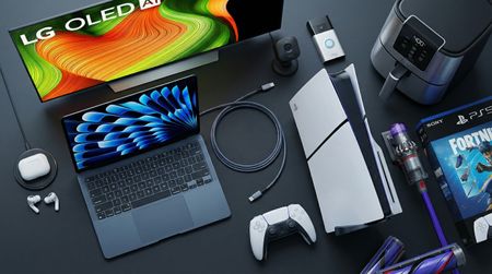 A collage of tech from the Best Buy Presidents' Day sale, including an LG TV, AirPods, PS5, Macbook, Dyson vacuum and Ninja air fryer on a black tabletop